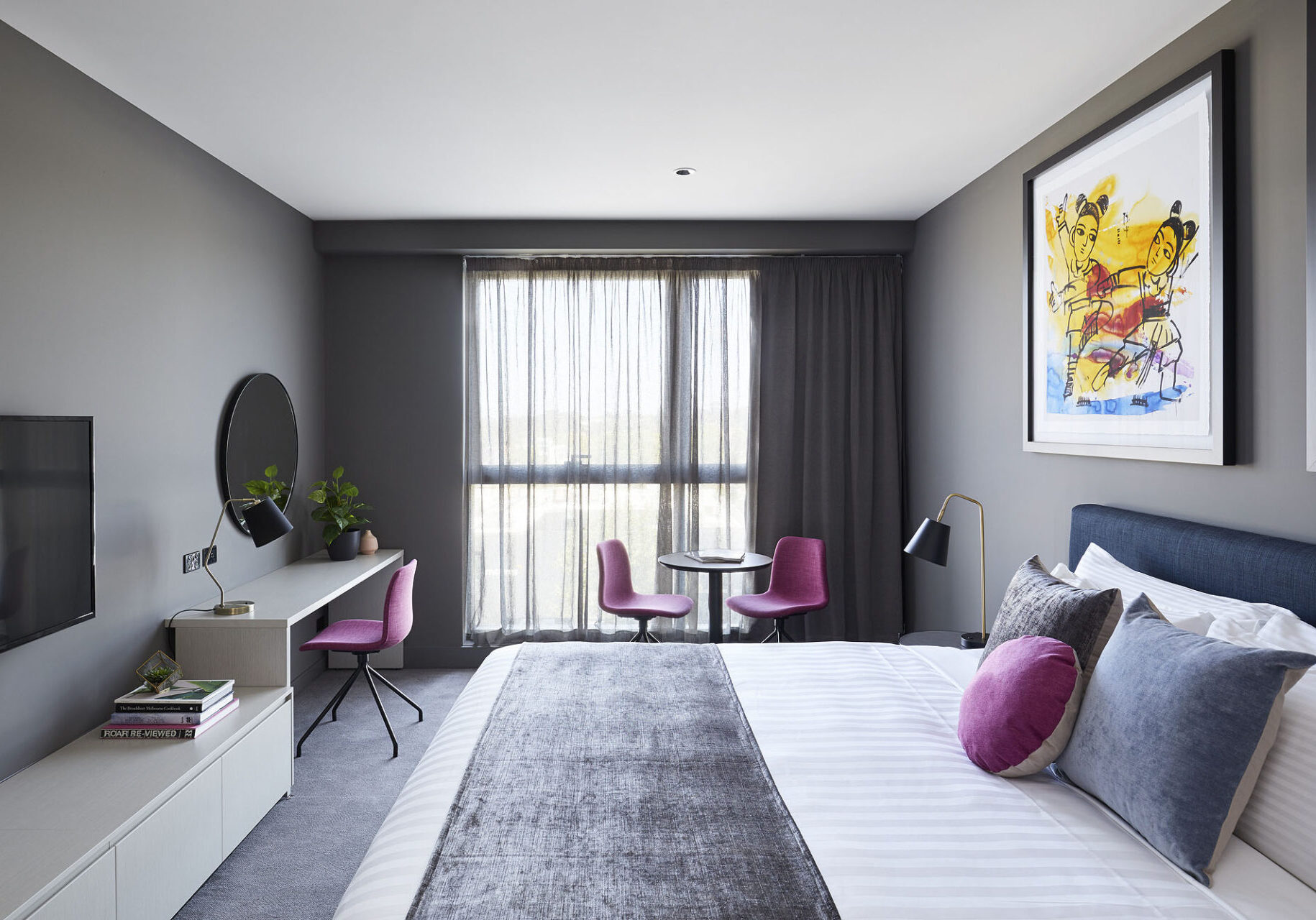 A hotel room featuring a queen bed, desk and chairs.